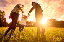 family of three in a field at sunset